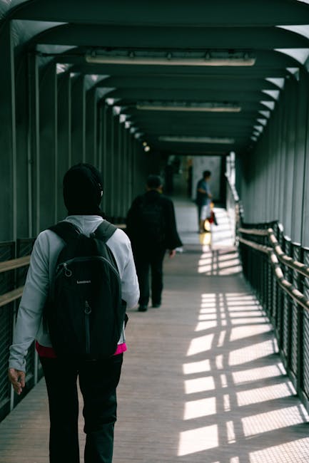 A spacious underground tunnel with a curved, tiled ceiling illuminated by evenly spaced bright white lights along the walls. The tunnel's surfaces are constructed from smooth, grey metallic panels, so